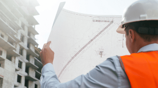 A construction manager holding up a blueprint of a road next to a buillding